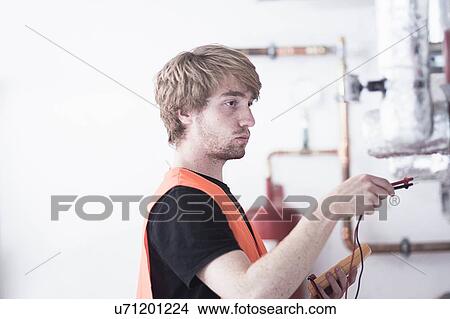 Side view of young man wearing high visability vest testing heating system View Large Photo Image Picture - Side view of young man wearing high visability vest testing heating system. Fotosearch