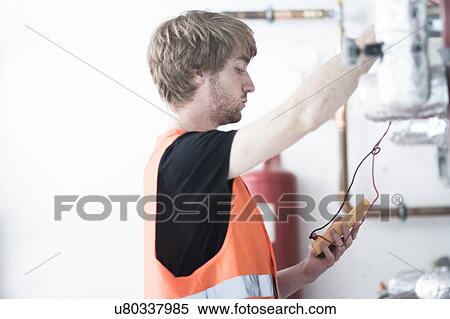 Stock Photography - Side view of young man wearing high visability vest testing heating system. Fotosearch