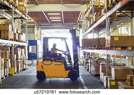 Stock Image - Silhouetted forklift truck at work in distribution warehouse. Fotosearch