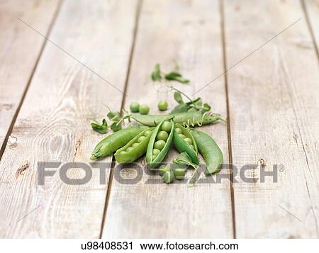 Stock Image - Still life of green peas in pods with pea shoots on wooden table. Fotosearch
