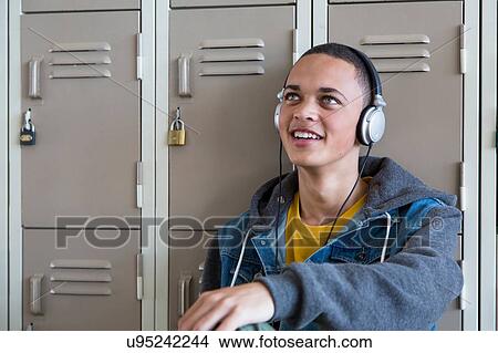 Picture - Student leaning against lockers, listening to music with headphones. Fotosearch