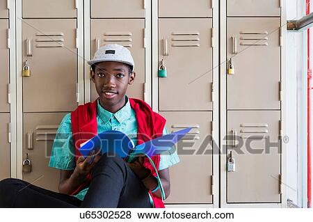 Stock Photo - Student leaning against lockers, looking up from textbook. Fotosearch