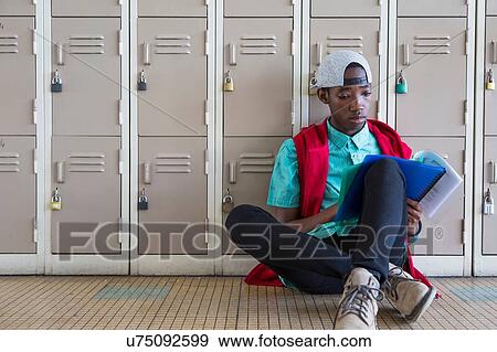 Stock Photo - Student leaning against lockers, reading textbook. Fotosearch