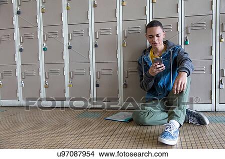 Picture - Student leaning against lockers, using smartphone. Fotosearch