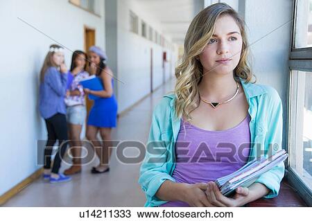 Stock Image - Student looking out window, friends gossiping in background. Fotosearch