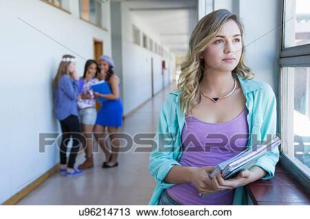 Stock Image - Student looking out window, friends gossiping in background. Fotosearch