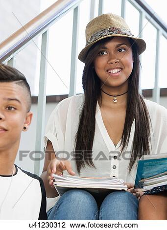 Stock Image - Students on steps, discussing over textbook. Fotosearch