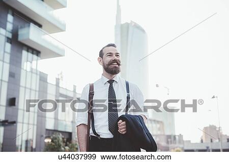 Stock Photo - Stylish bearded businessman carrying jacket walking in city. Fotosearch