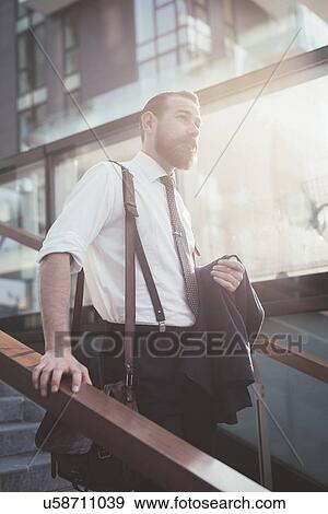 Stock Photo - Stylish businessman carrying jacket moving down city stairway. Fotosearch