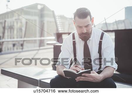 Stock Photograph - Stylish businessman making diary notes from smartphone on city seat. Fotosearch
