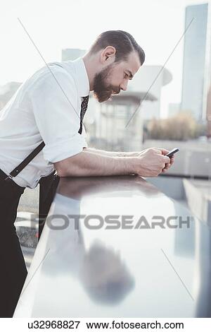 Stock Photo - Stylish businessman reading smartphone text leaning against office balcony. Fotosearch