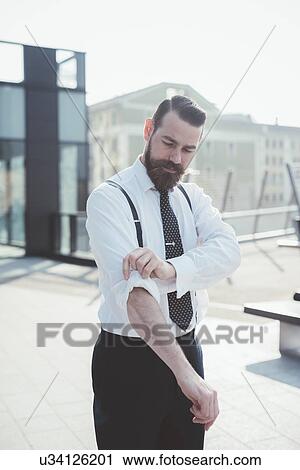 Stylish businessman rolling up sleeves on footbridge View Large Photo Image Stock Image - Stylish businessman rolling up sleeves on footbridge. Fotosearch