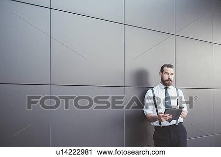 Stylish businessman using digital tablet and smartphone leaning against office wall View Large Photo Image Stock Image - Stylish businessman using digital tablet and smartphone leaning against office wall. Fotosearch