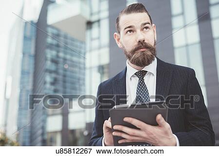 Stock Photo - Stylish businessman using digital tablet touchscreen outside office. Fotosearch