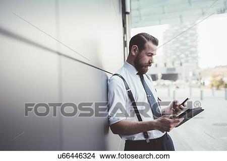 Stylish businessman using smartphone and digital tablet outside office View Large Photo Image Picture - Stylish businessman using smartphone and digital tablet outside office. Fotosearch