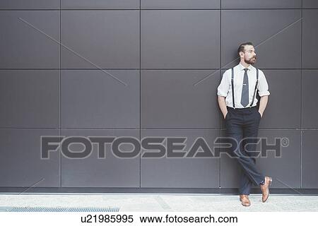 Stylish businessman with hands in pockets leaning against office wall View Large Photo Image Stock Photography - Stylish businessman with hands in pockets leaning against office wall. Fotosearch