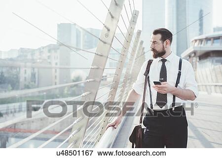 Stylish businessman with smartphone looking out from city footbridge View Large Photo Image Stock Photo - Stylish businessman with smartphone looking out from city footbridge. Fotosearch