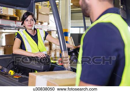 Stock Image - Supervisor instructing female forklift truck driver in distribution warehouse. Fotosearch