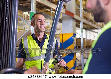 Stock Photo - Supervisor instructing male forklift truck driver in distribution warehouse. Fotosearch