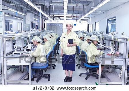 Stock Image - Supervisor overseeing quality check station at factory producing flexible electronic circuit boards. Plant is located in the south of China, in Zhuhai, Guangdong province. Fotosearch