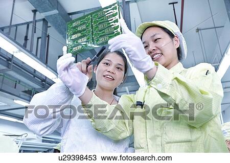 Stock Image - Supervisor overseeing work at quality check station at factory producing flexible electronic circuit boards. Plant is located in the south of China, in Zhuhai, Guangdong province. Fotosearch