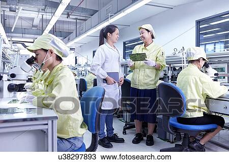 Stock Image - Supervisor overseeing work at quality check station at factory producing flexible electronic circuit boards. Plant is located in the south of China, in Zhuhai, Guangdong province. Fotosearch