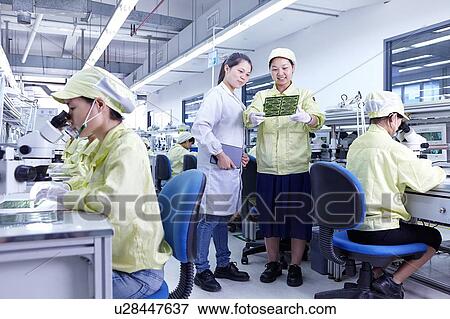 Stock Photo - Supervisor overseeing work at quality check station at factory producing flexible electronic circuit boards. Plant is located in the south of China, in Zhuhai, Guangdong province. Fotosearch
