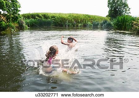 Stock Image - Teenage boy and sister splashing in rural lake. Fotosearch