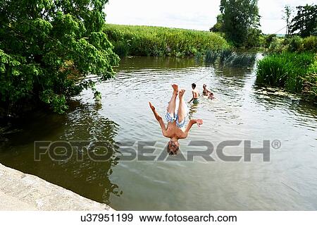 Stock Photo - Teenage boy somersaulting into rural lake. Fotosearch