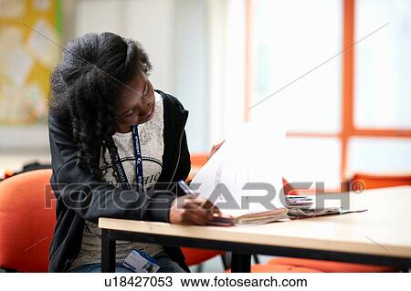 Stock Image - Teenage female student writing in file. Fotosearch