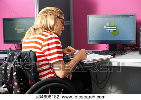 Stock Image - Teenage girl in wheelchair writing up file notes in class. Fotosearch