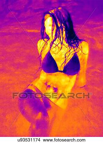 Picture - Thermal image of mid adult woman wearing bikini sitting on beach. Fotosearch
