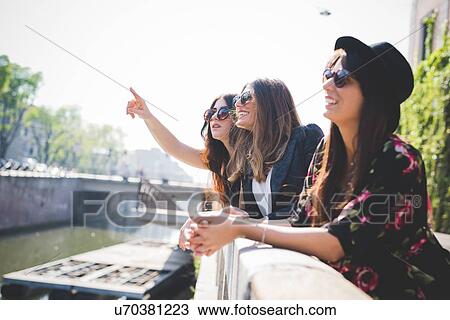 Three stylish young female friends looking up from city riverside View Large Photo Image Stock Image - Three stylish young female friends looking up from city riverside. Fotosearch