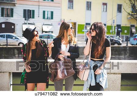 Three stylish young female friends chatting at city riverside View Large Photo Image Stock Image - Three stylish young female friends chatting at city riverside. Fotosearch