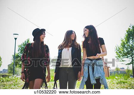 Three young female friends chatting whilst strolling in park View Large Photo Image Stock Image - Three young female friends chatting whilst strolling in park. Fotosearch