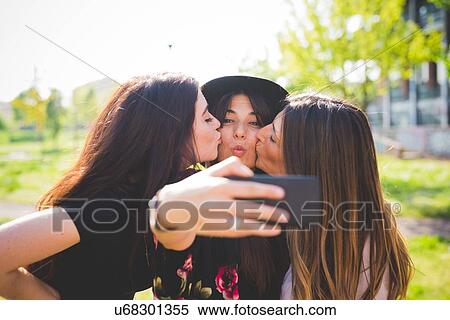 Three young female friends cheek kissing for smartphone selfie in park View Large Photo Image Stock Photography - Three young female friends cheek kissing for smartphone selfie in park. Fotosearch