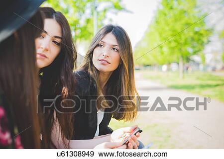 Stock Photo - Three young female friends having conversation in park. Fotosearch