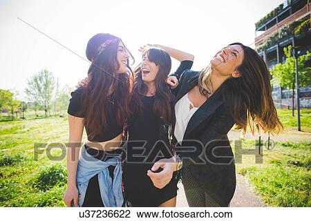 Stock Image - Three young female friends laughing together in park. Fotosearch