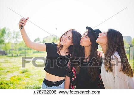 Three young female friends puckering lips for smartphone selfie in park View Large Photo Image Stock Photograph - Three young female friends puckering lips for smartphone selfie in park. Fotosearch
