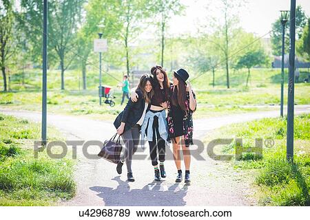 Stock Photo - Three young female friends strolling together in park. Fotosearch