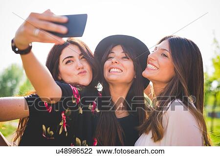 Three young female friends taking smartphone selfie in park View Large Photo Image Stock Image - Three young female friends taking smartphone selfie in park. Fotosearch