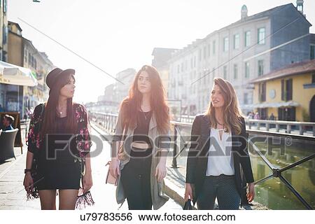 Stock Photograph - Three young stylish women strolling on canal waterfront. Fotosearch