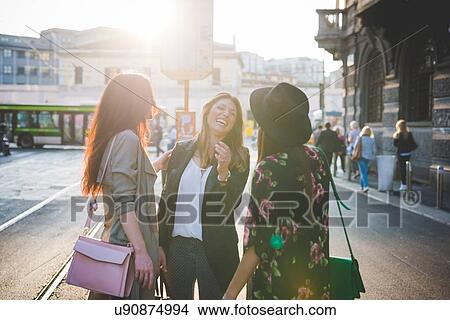Three young women chatting and laughing on city street View Large Photo Image Picture - Three young women chatting and laughing on city street. Fotosearch