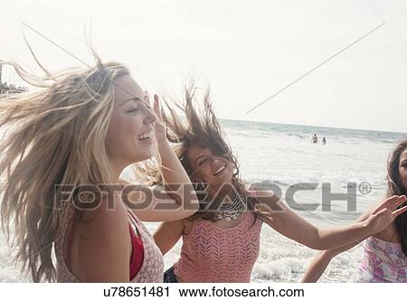 Stock Image - Three young women fooling around on windswept beach. Fotosearch