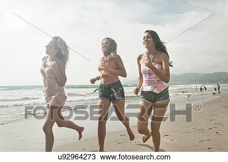 Stock Image - Three young women fun running along beach. Fotosearch