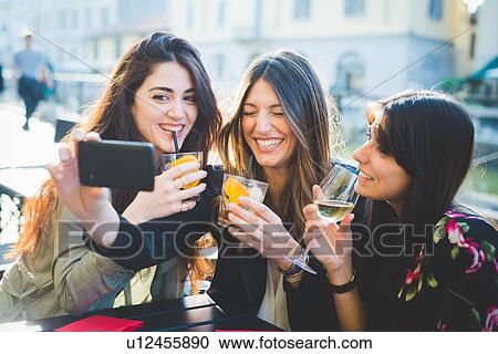 Three young women giggling for smartphone selfie at waterfront cafe View Large Photo Image Stock Image - Three young women giggling for smartphone selfie at waterfront cafe. Fotosearch