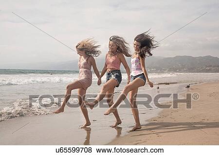 Stock Photo - Three young women holding hands and dancing on windswept beach. Fotosearch