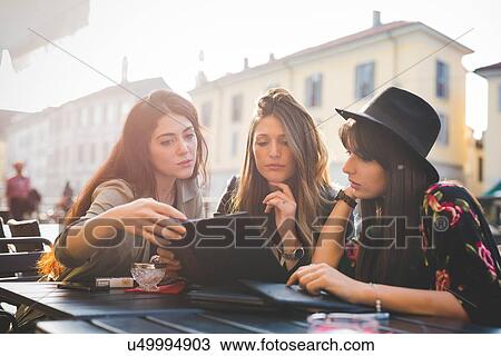 Three young women reading update on digital tablet at sidewalk cafe View Large Photo Image Stock Image - Three young women reading update on digital tablet at sidewalk cafe. Fotosearch