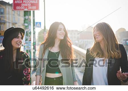 Stock Photograph - Three young women strolling and chatting in city. Fotosearch