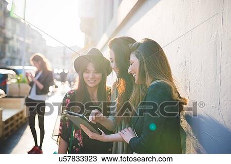 Three young women using digital tablet on city street View Large Photo Image Stock Image - Three young women using digital tablet on city street. Fotosearch